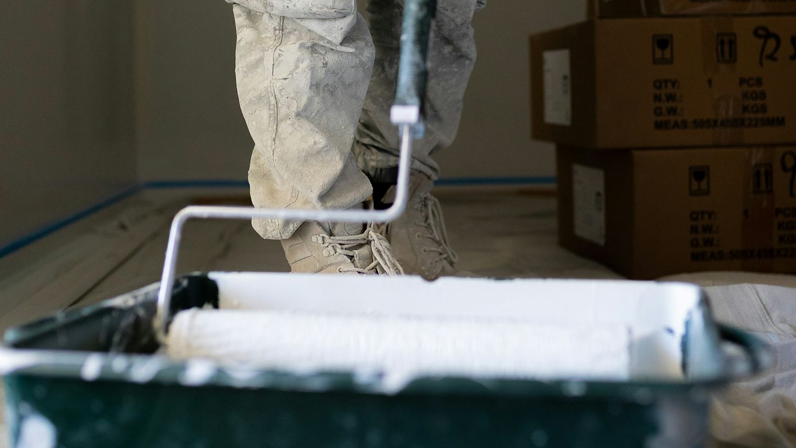 Painter loading a roller from a paint tray in a room with moving boxes